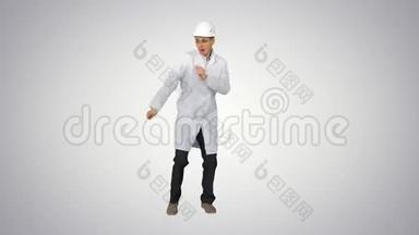 有趣的Scientinst穿着<strong>白色</strong>长袍和安全帽在<strong>渐变背景</strong>下跳舞。